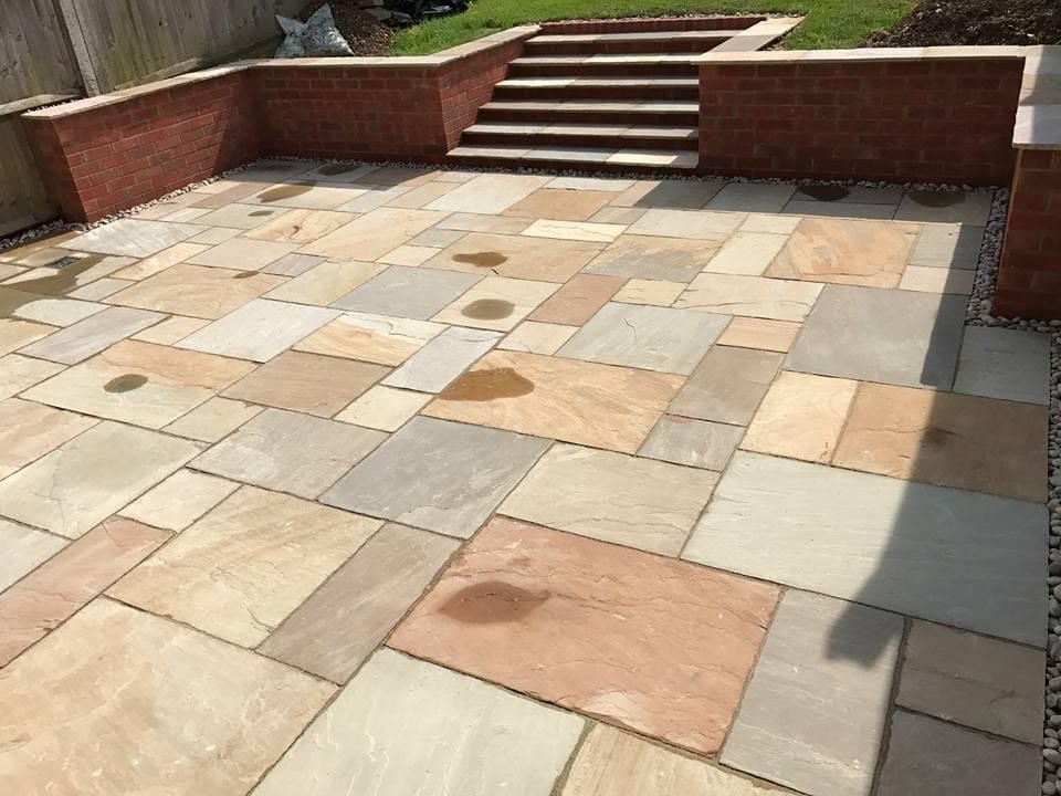 Patio with multicolored stone pavers and brick retaining walls with steps in a residential garden setting
