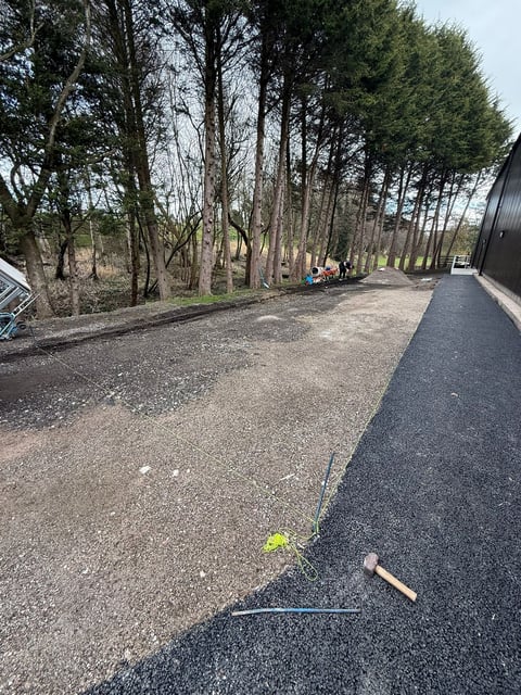 Tennis racket and ball on asphalt path with trees and person in background at park or recreational area