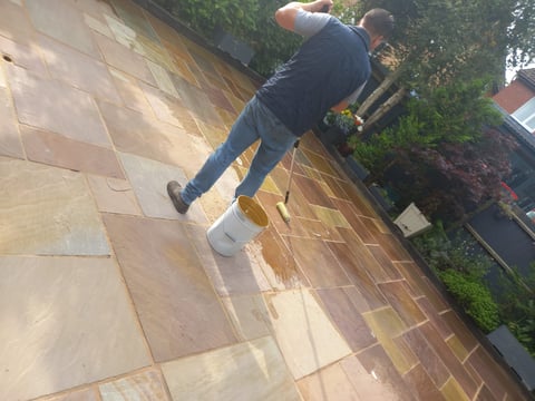 Person mowing a flagstone patio with a lawn mower on a sunny day