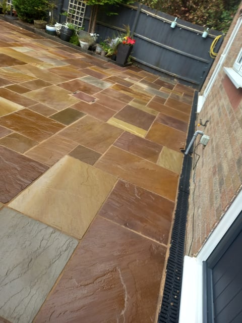 Patio with varied brown and tan stone tiles, potted plants along fence, and garden containers in background