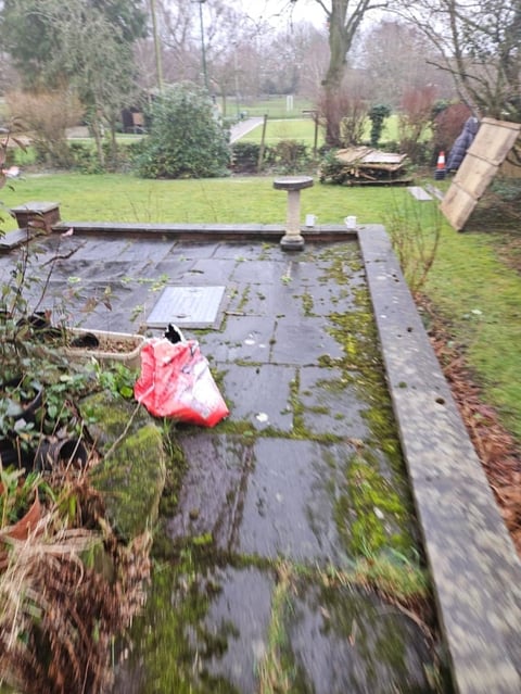 Wet patio with pink cloth and green moss covering stone pavers in overgrown garden yard