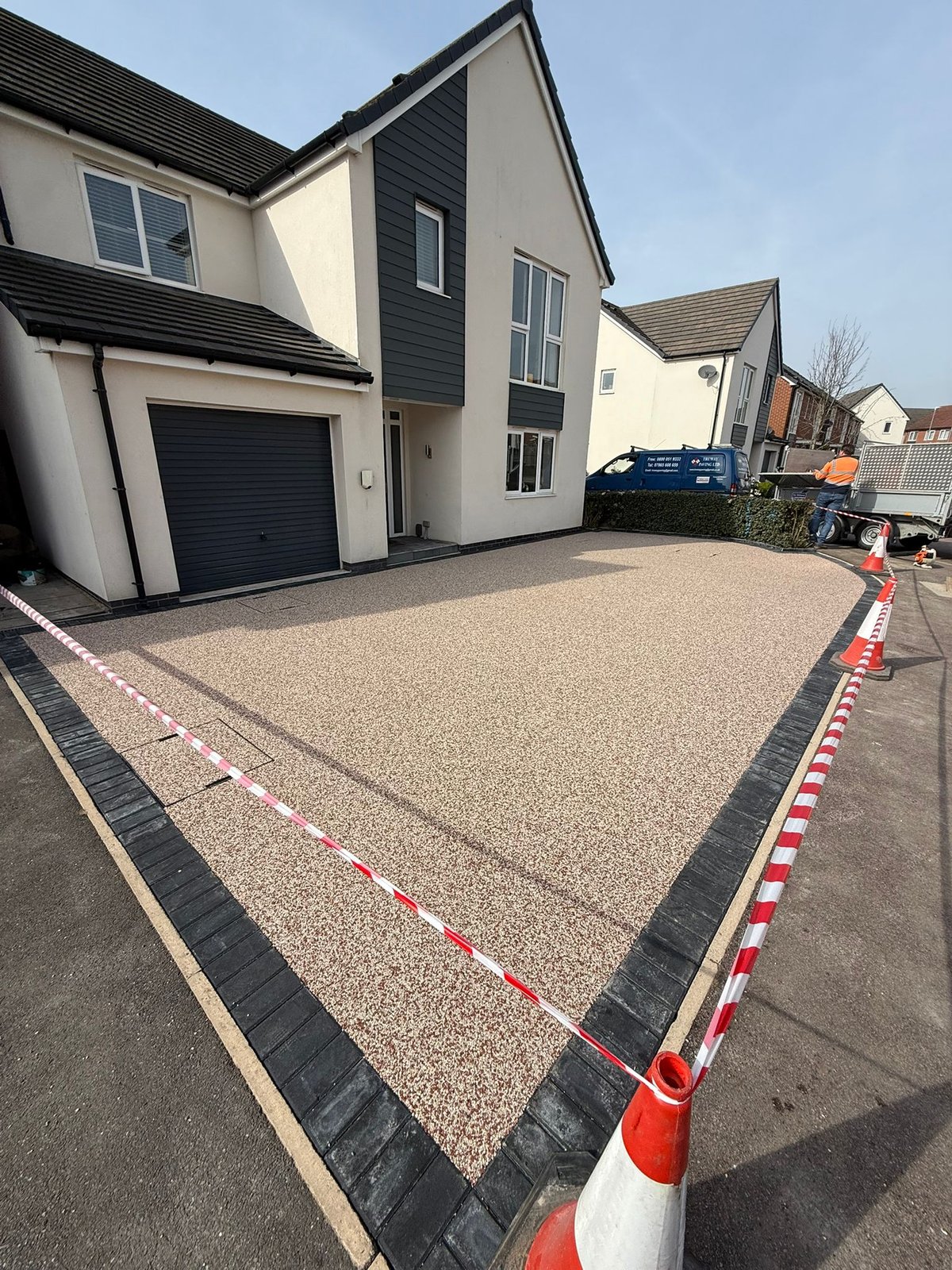 New paved driveway with black border and red and white safety tape marking, modern two-story house with garage
