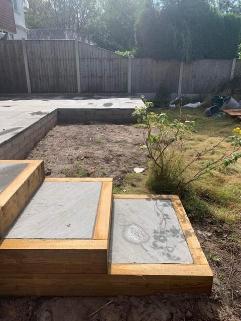 Backyard garden beds under construction with wooden frames and concrete covers, wooden fence and raised planter boxes visible