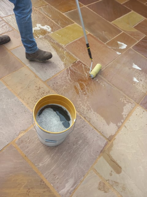 Person cleaning tiled floor with a brush and bucket of water during home renovation or maintenance work