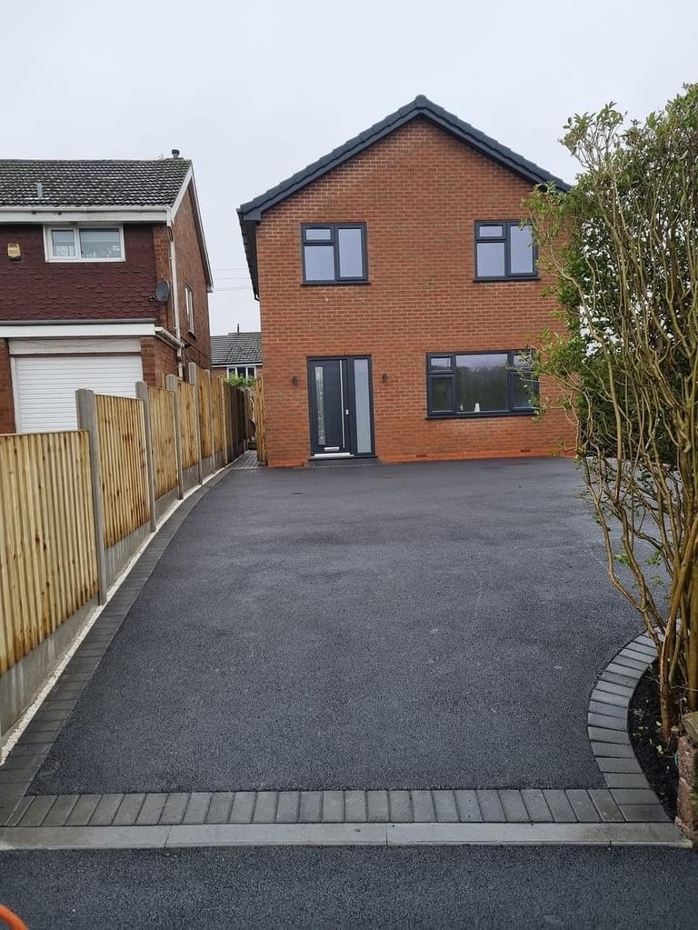 Modern brick house with dark roof and driveway, featuring contemporary windows and landscaping