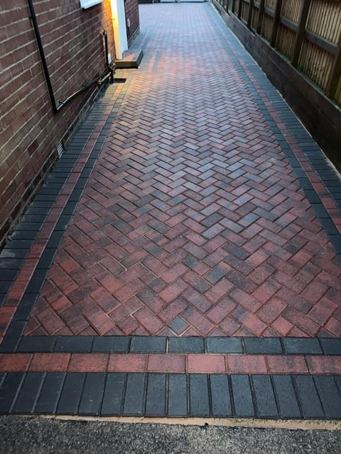 Narrow paved alleyway with red and dark brick herringbone pattern bordered by metal gates and brick walls