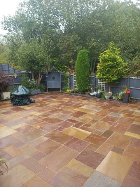 Backyard patio with terra-cotta tiles, garden structures, tall green trees, potted plants, and shrubs