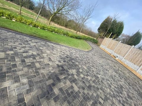 Paved patio with herringbone pattern pavers, bordered by green lawn, bare trees, and wooden fence