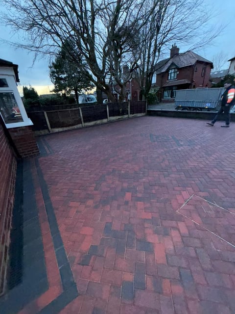 Brick paved town square at dusk with bare trees, residential buildings, and people in the background