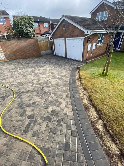 Brick house with white double garage doors and herringbone paved driveway next to green lawn