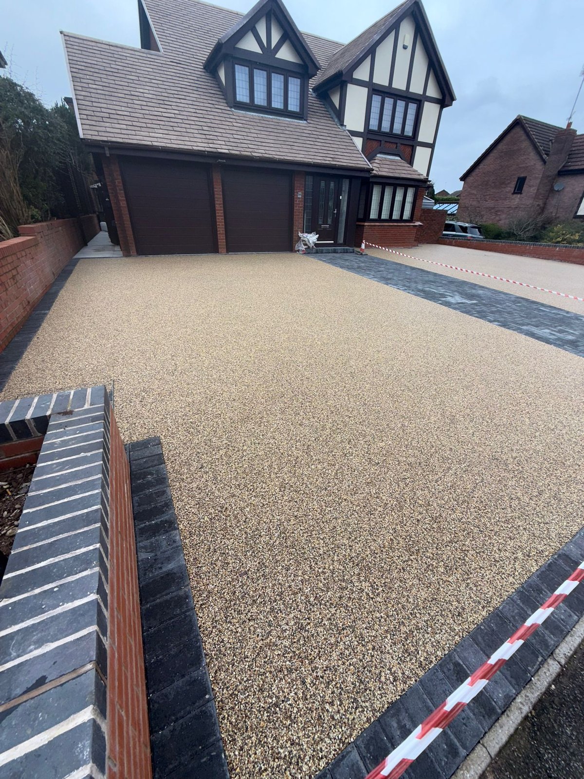 Tudor-style house with black and white half-timbered upper floors, dark garage doors, and large gravel driveway with decorative border edging