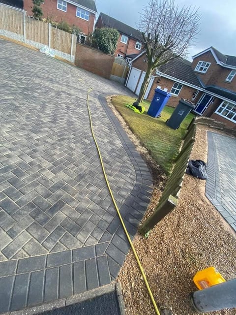 Residential driveway with yellow hose, brick townhouses, and blue waste bins along the street