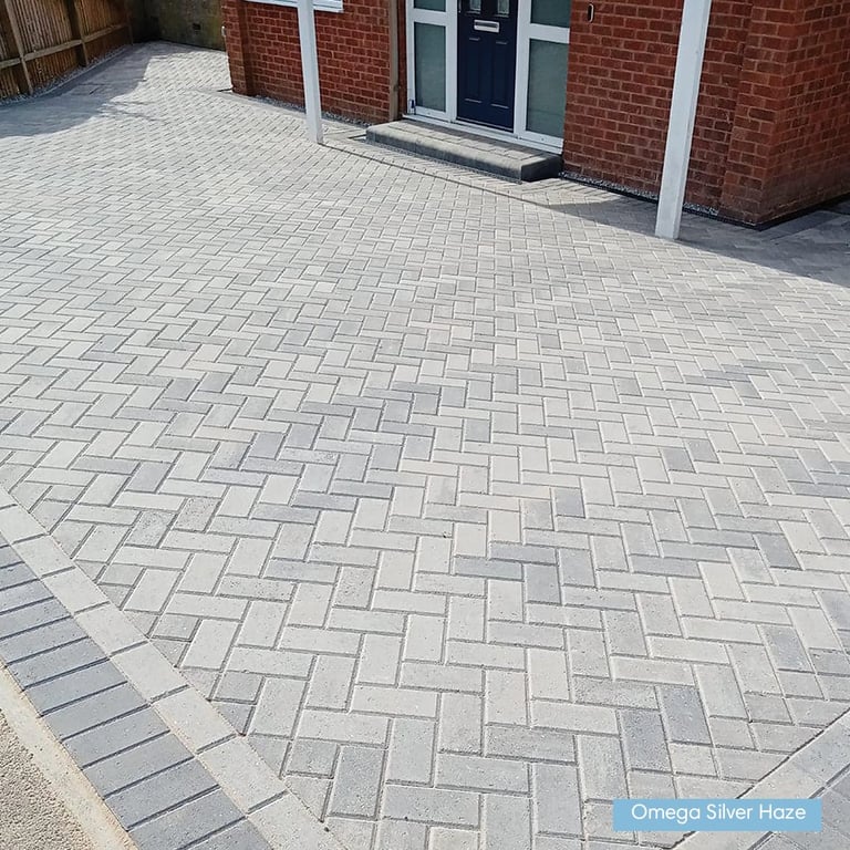 Herringbone patterned paved driveway in front of a brick building with dark doors and white trim