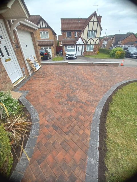 Brick paver driveway in suburban residential street with Tudor-style homes and parked cars