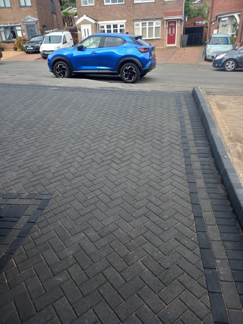 Blue SUV parked on brick-paved driveway in front of brick residential houses