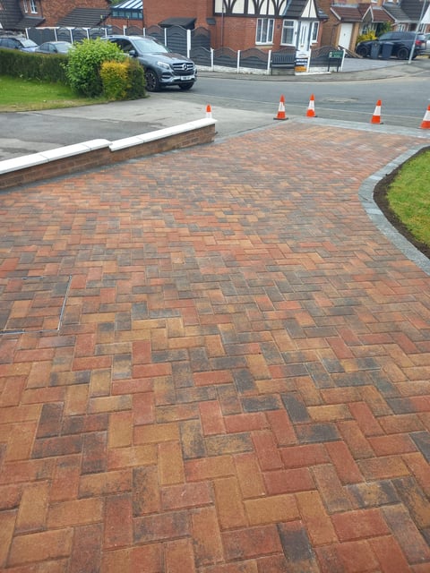 Newly laid brick paver driveway with herringbone pattern, traffic cones, and residential buildings in background