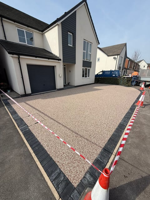 Modern two-story house with cream and dark exterior, newly installed gravel driveway with black borders, black garage door, and safety barriers visible on street