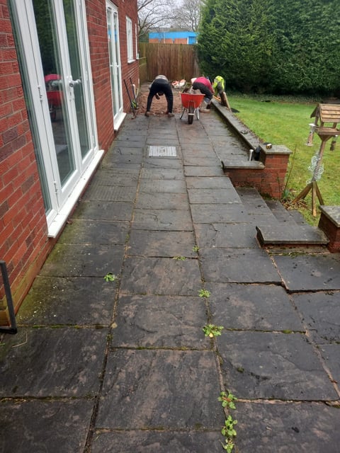 Children playing on a backyard patio beside a brick house with a lawn and garden